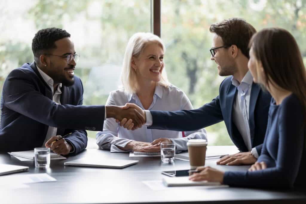 Smiling diverse businesspeople shake hands get acquainted greeting at team meeting in office